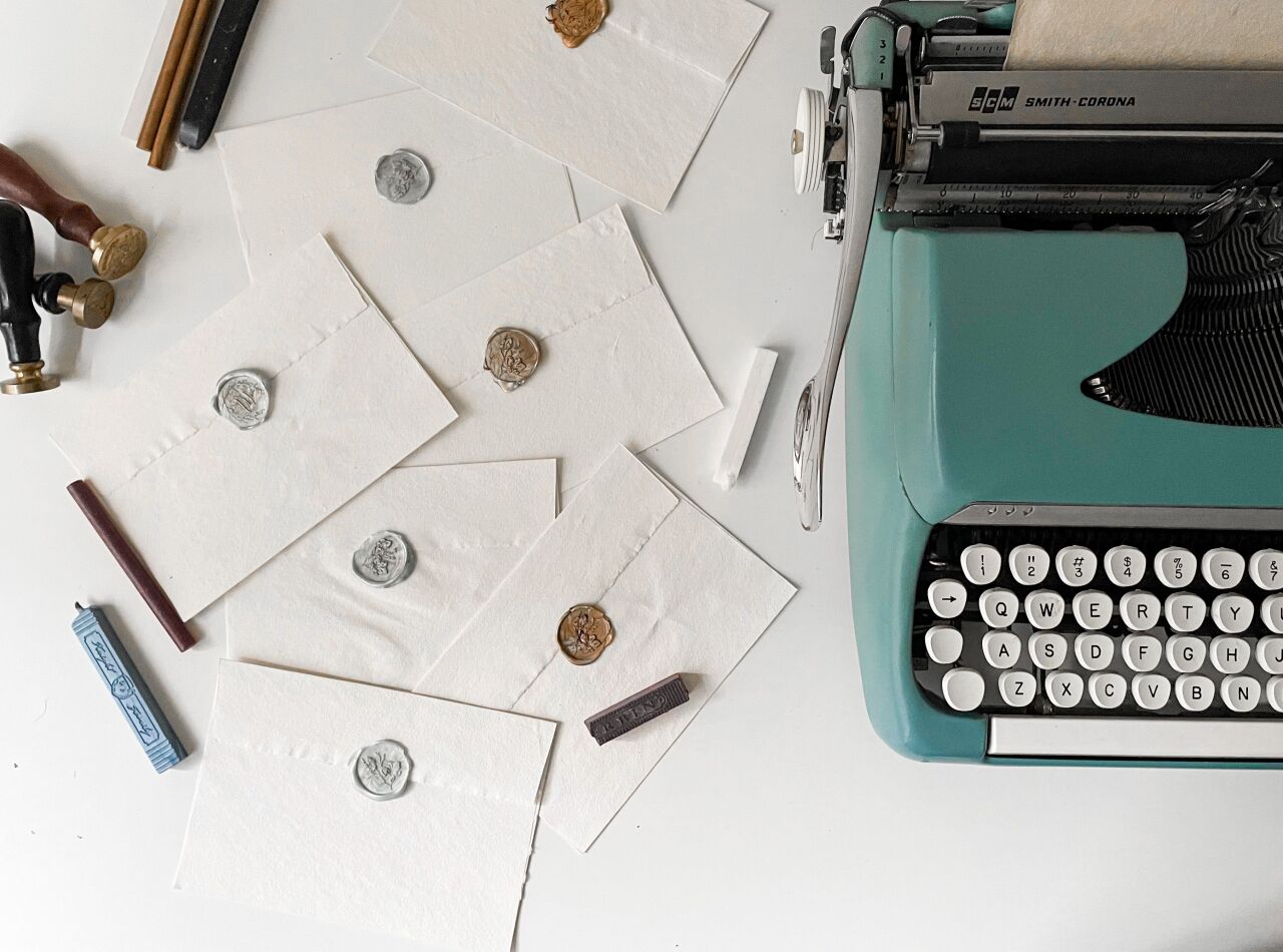 A mint typewriter beside a pile of wax-sealed envelopes on a white desk