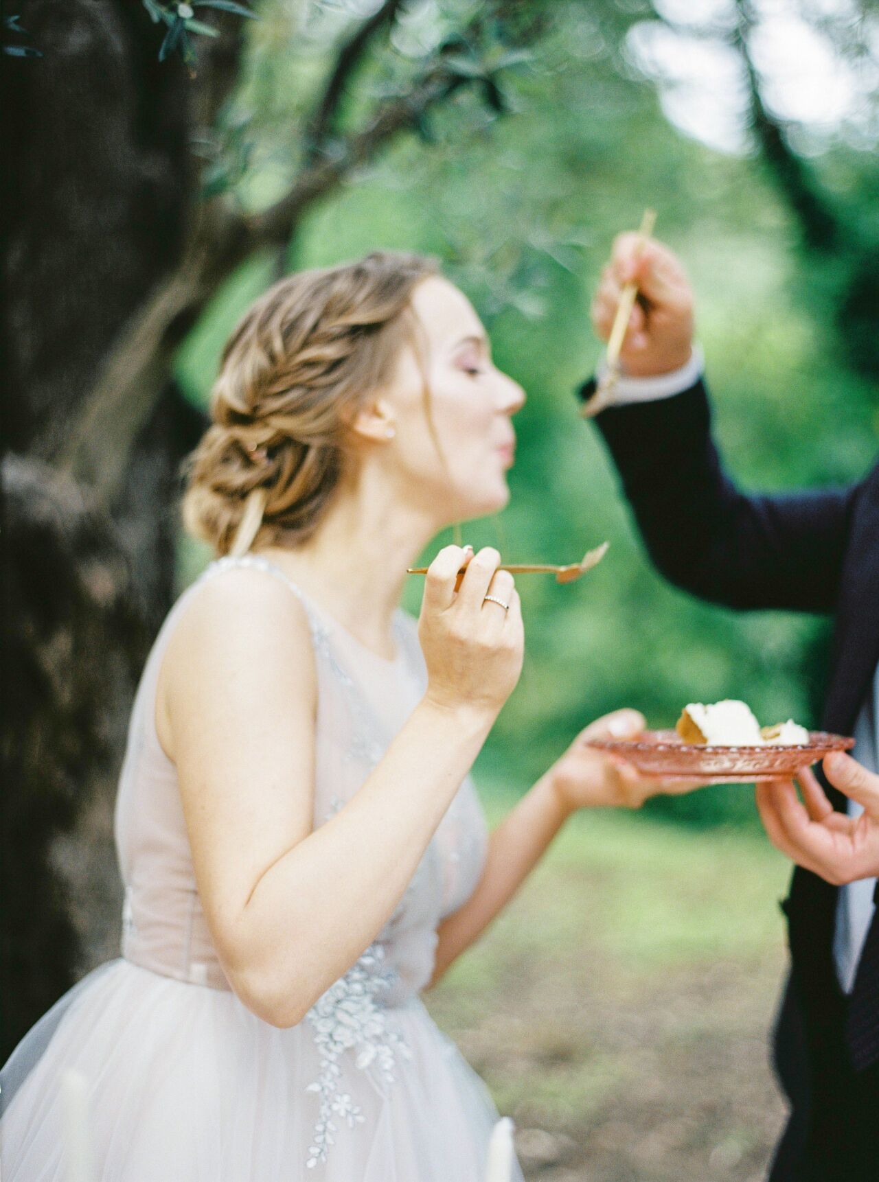 Bride tasting a forkful of wedding cake beneath the olive trees