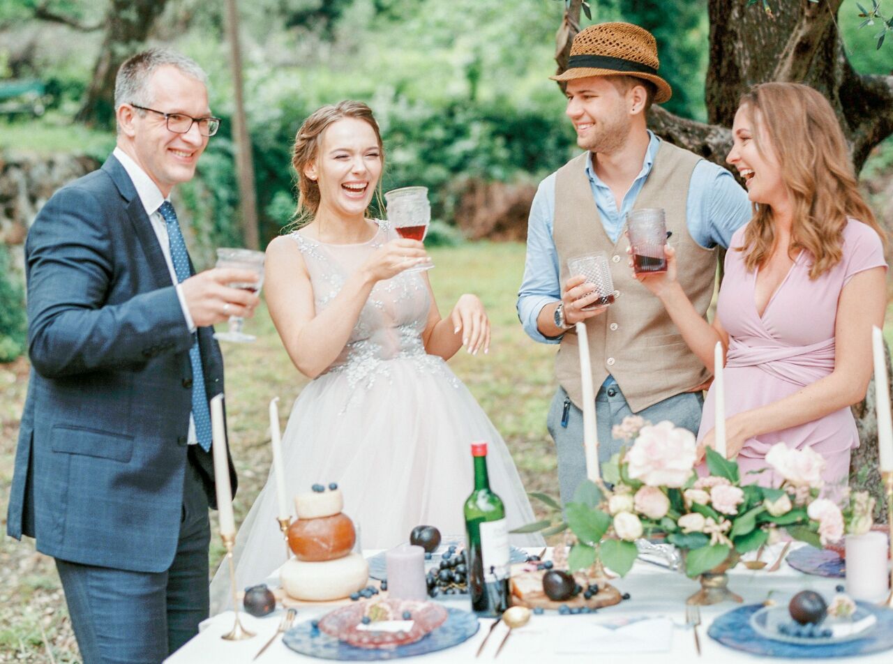 Bride laughing and clinking glasses with friends across a candlelit garden table