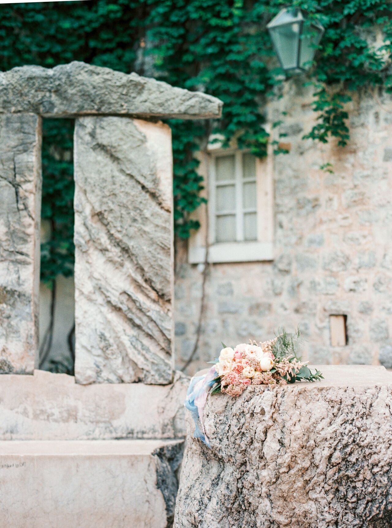 Blush and peach bridal bouquet with trailing blue ribbons resting on a weathered stone wall