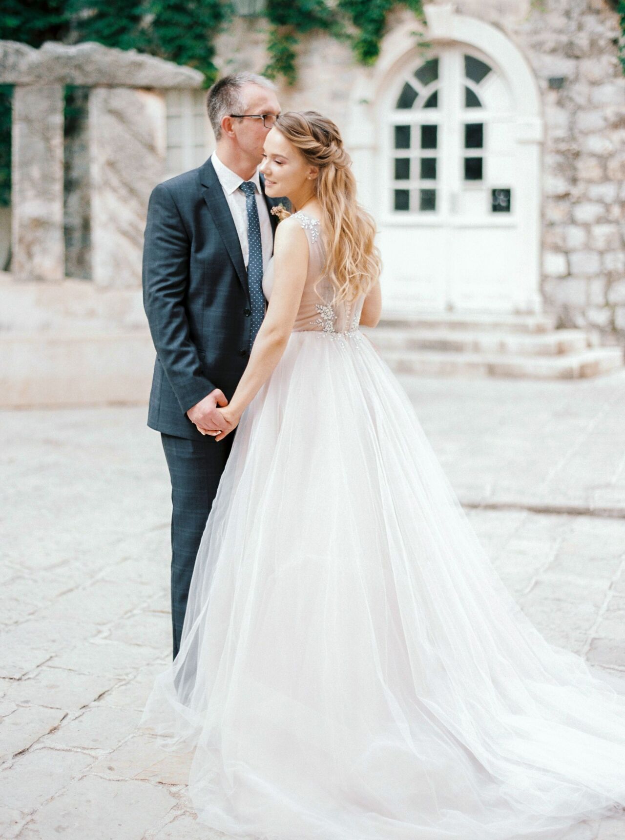 Groom kissing the bride outside a pale stone building with arched windows