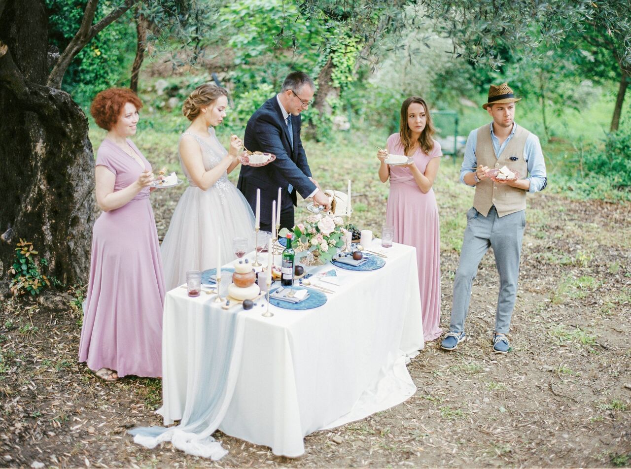 Friends in dusty pink gathered around a long white reception table in an olive grove
