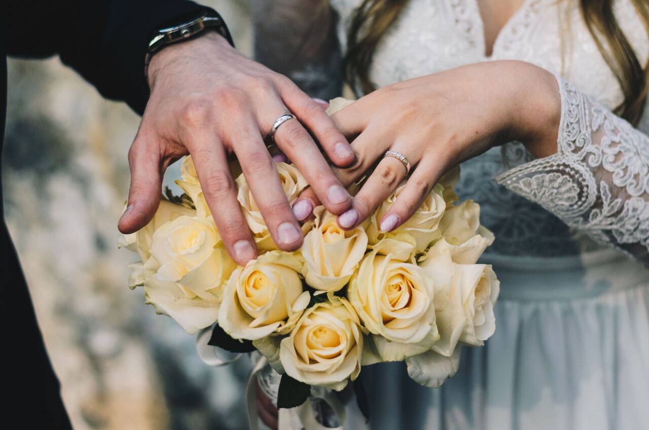 Couple's hands wearing wedding rings, resting on a bouquet of cream roses