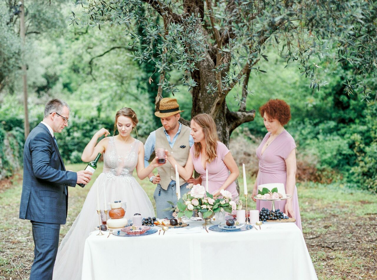 Groom pouring drinks at a garden reception table as the bride and friends raise their glasses