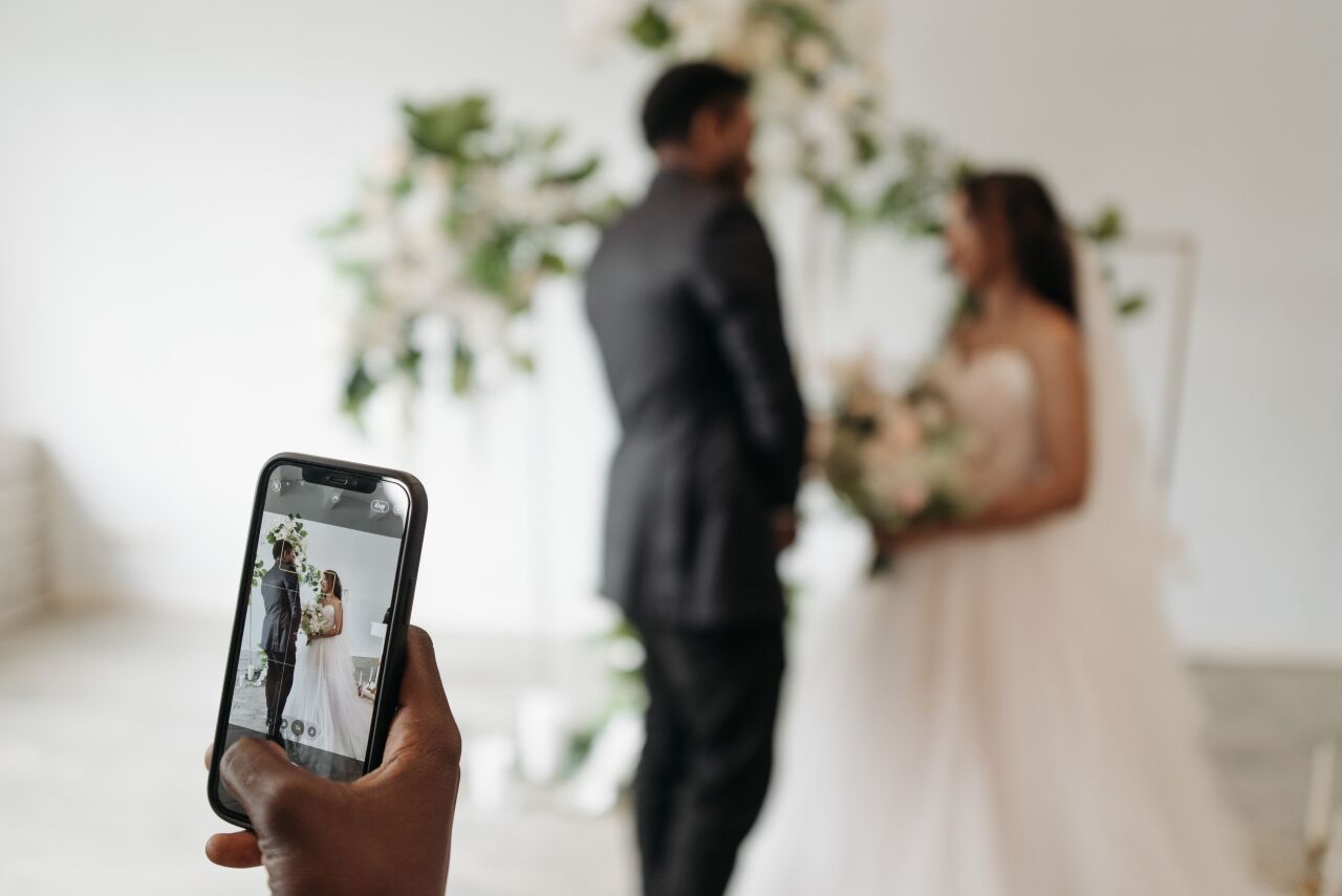 A guest's phone held up, recording the bride and groom at the altar