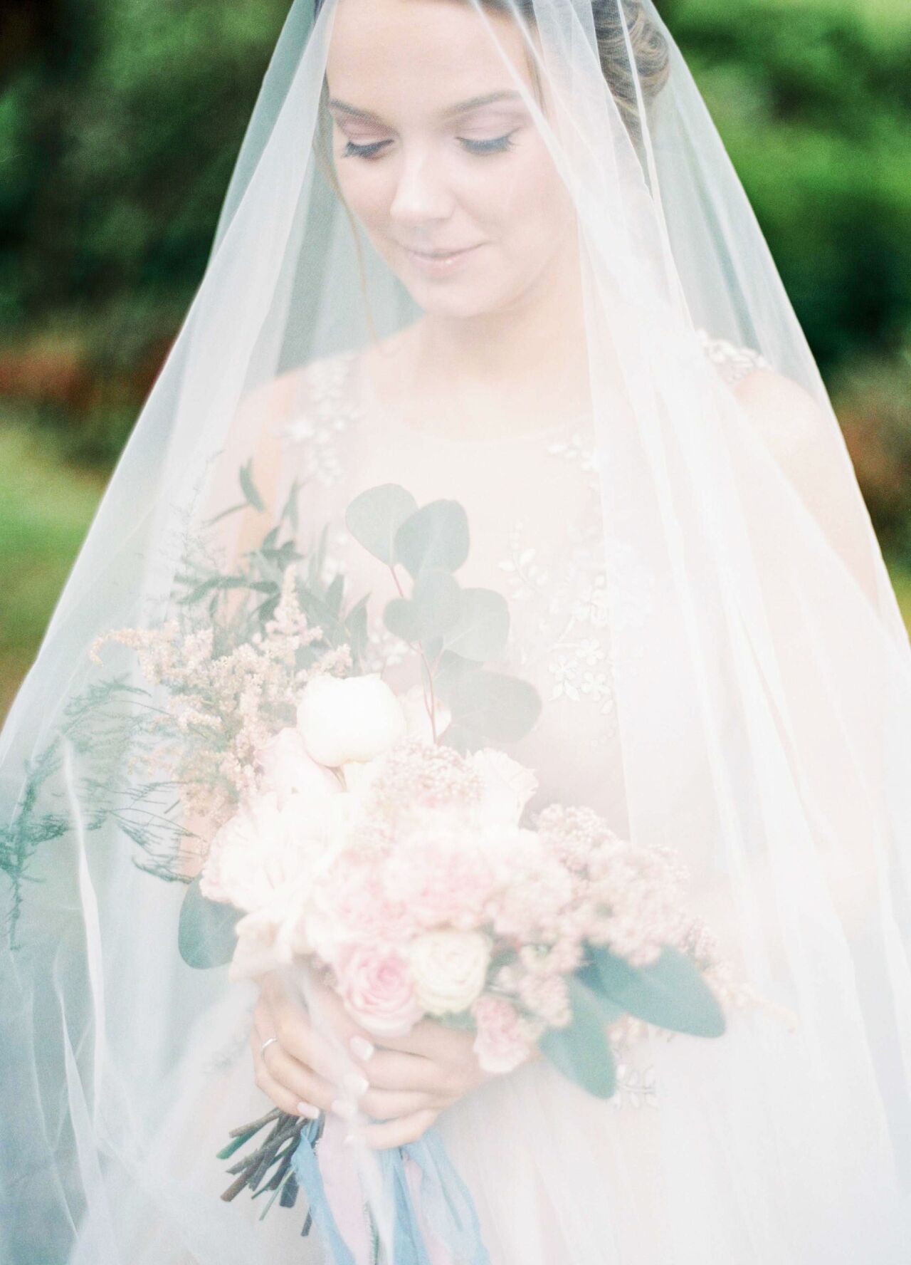 Bride holding a blush rose bouquet beneath a soft, sheer veil