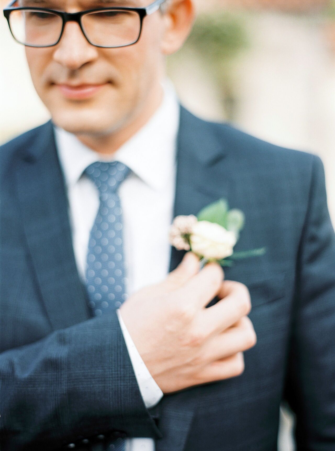 Groom adjusting the blush rose boutonniere on his navy lapel