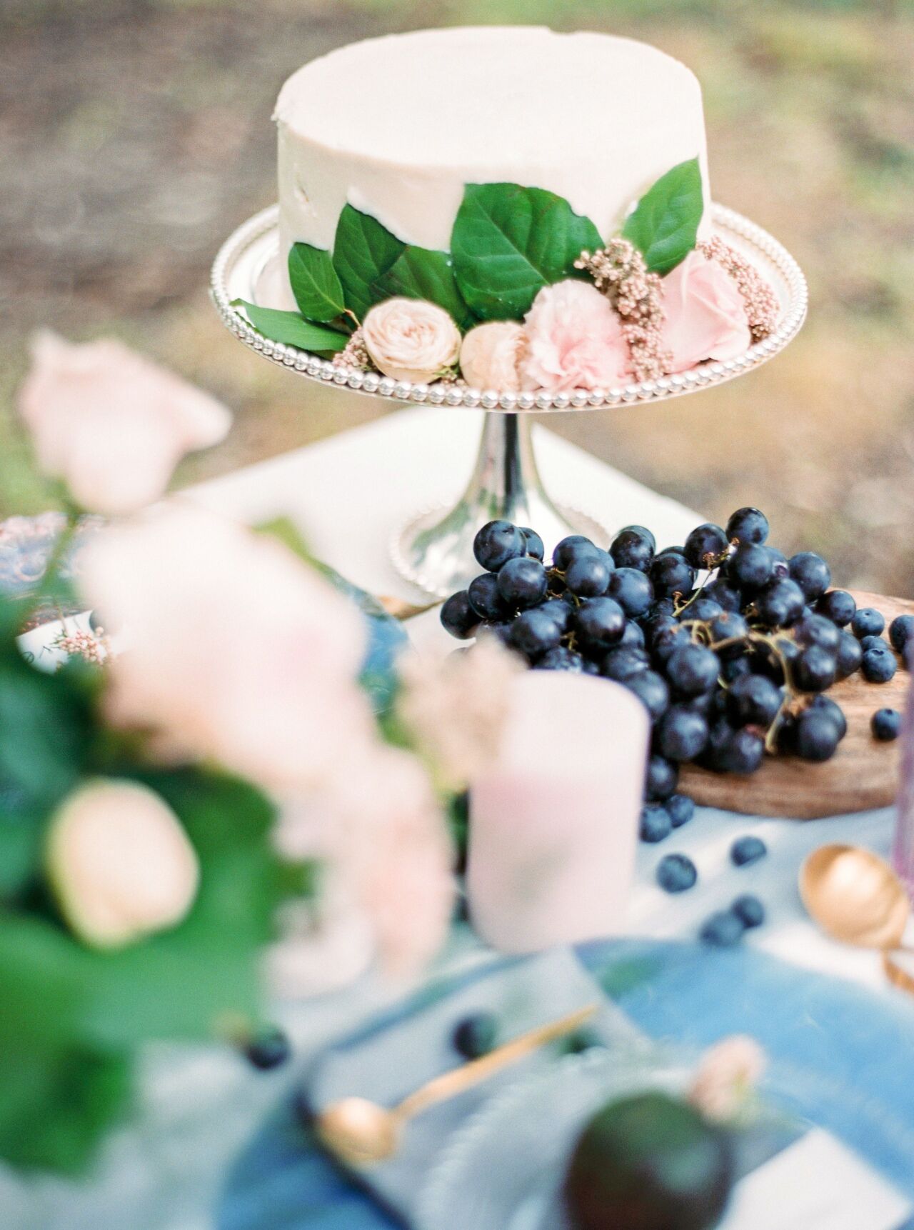 White wedding cake topped with blush roses beside bowls of grapes and blueberries