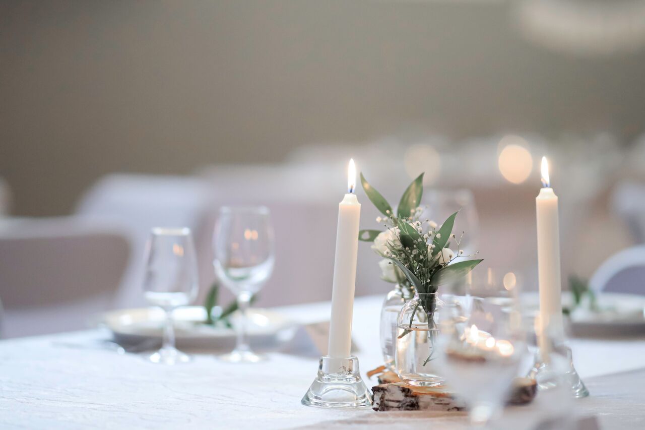Candles, wine glasses and a small posy on a white table in soft daylight