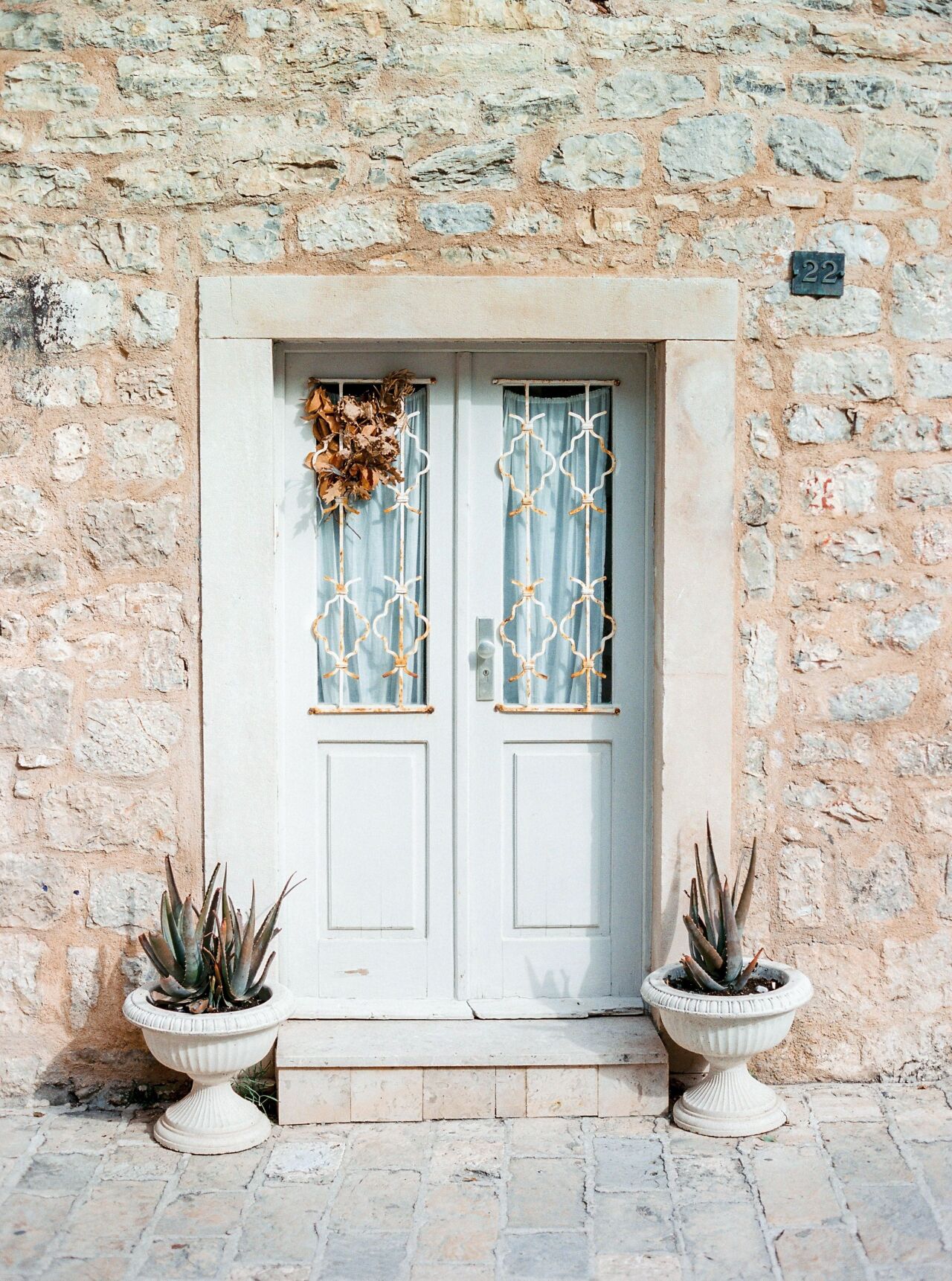 White double door framed by pale stone and potted plants in Budva's old town