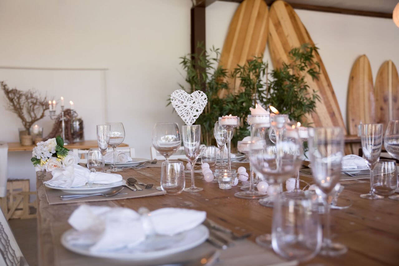 Long reception table in a white pavilion set with glassware, white napkins and a woven heart