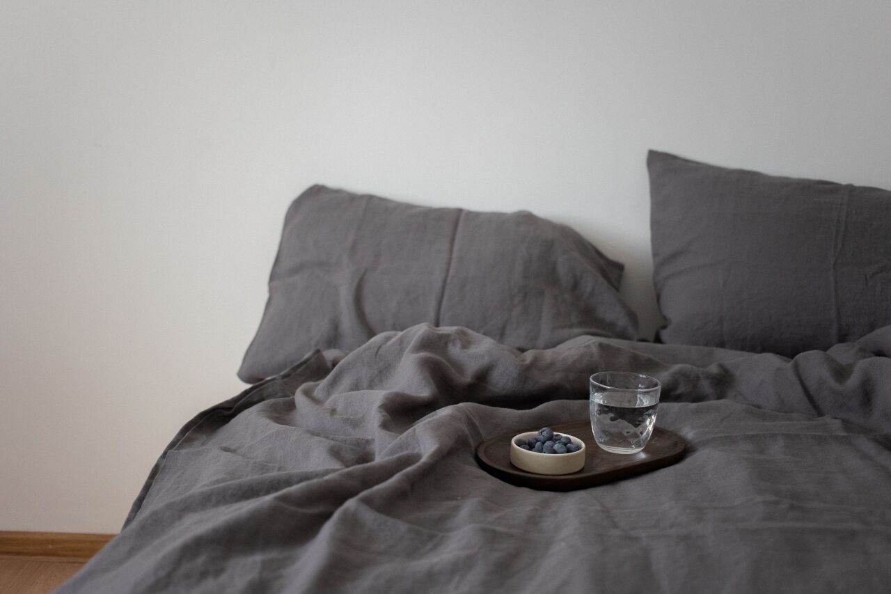 Rumpled charcoal linen bedding with a small tray and a glass of water