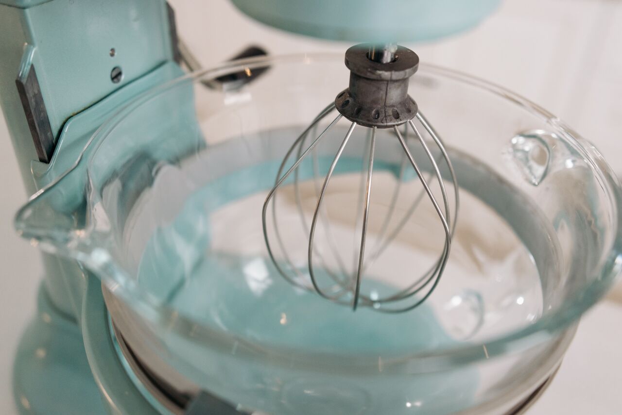 Close-up of a pale mint stand mixer's glass bowl and wire whisk in a bright kitchen