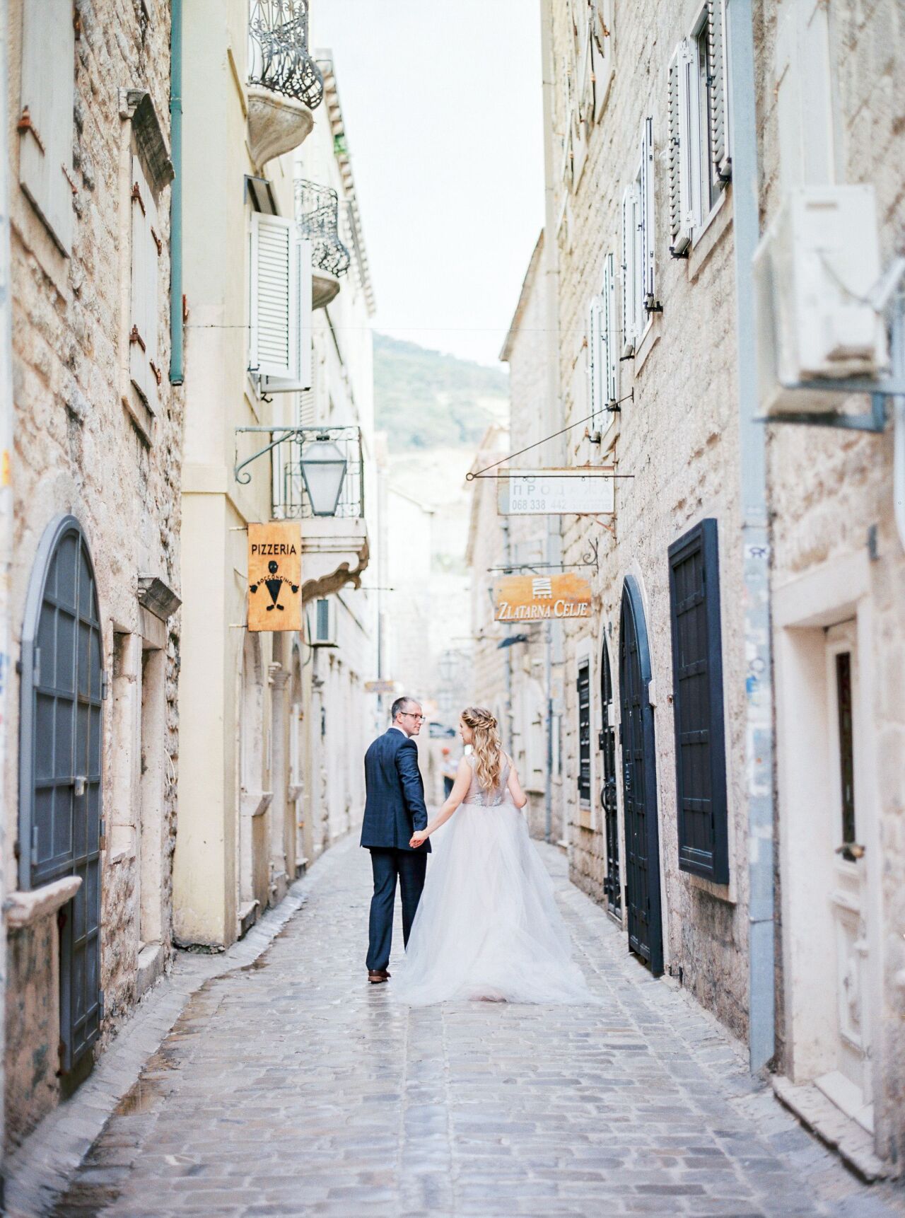 Bride and groom walking hand in hand down a narrow cobbled lane between old stone buildings